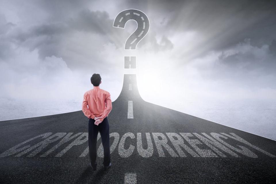 Person standing on a highway marked Cryptocurrency, looking at the road forming a giant question mark in the sky.